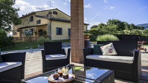 An outdoor patio area with wicker furniture and a glass table, overlooking a house with a brick pillar and a wooden fence. - Il Nido di Gabbiano (Scarperia e San Piero)
