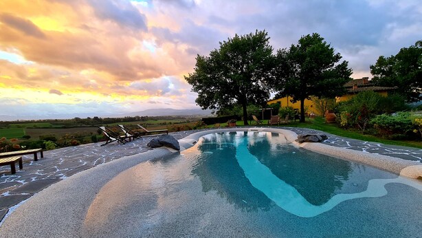 A swimming pool with a stone deck and lounge chairs, surrounded by trees and a view of the countryside. - Il Nido di Gabbiano (Scarperia e San Piero)