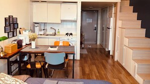 A compact studio apartment with a kitchenette, a dining area, a small office space, and a staircase leading to an upper level. - Travel House (Seoul)