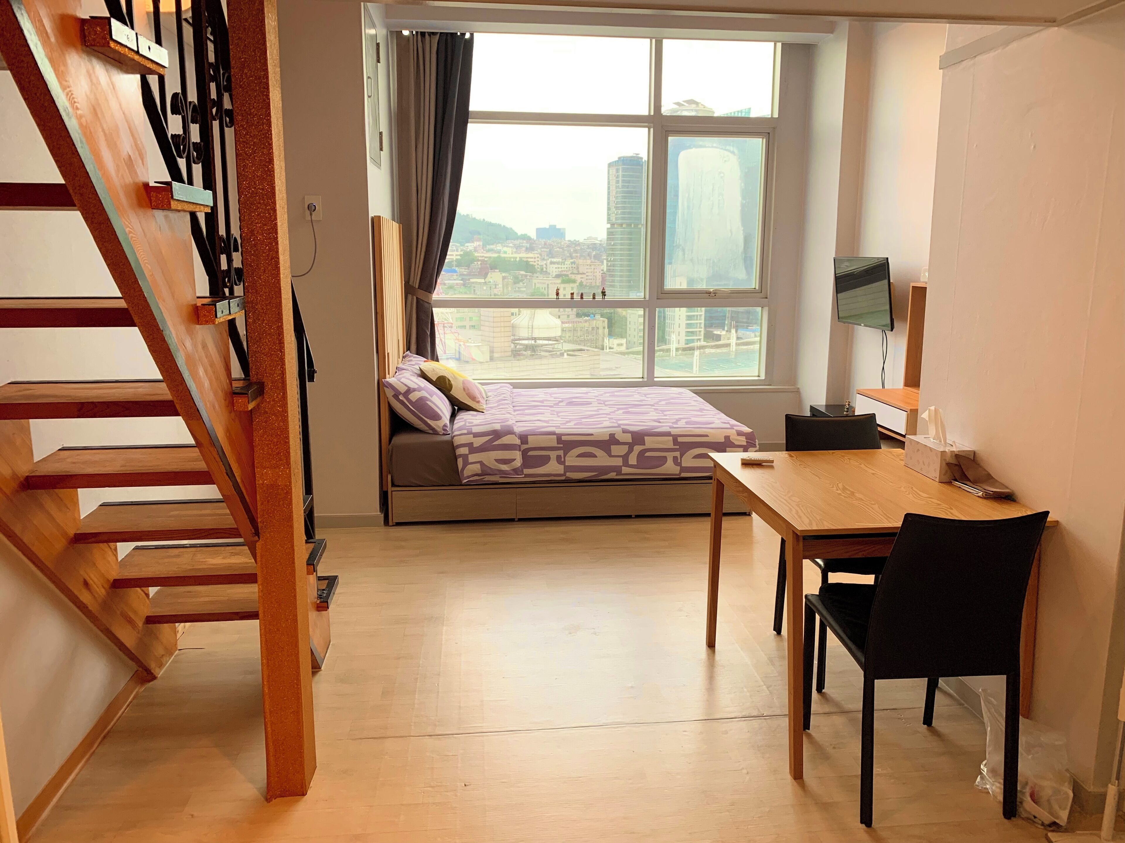 Un dormitorio con cama, escritorio y ventana con vista a la ciudad.