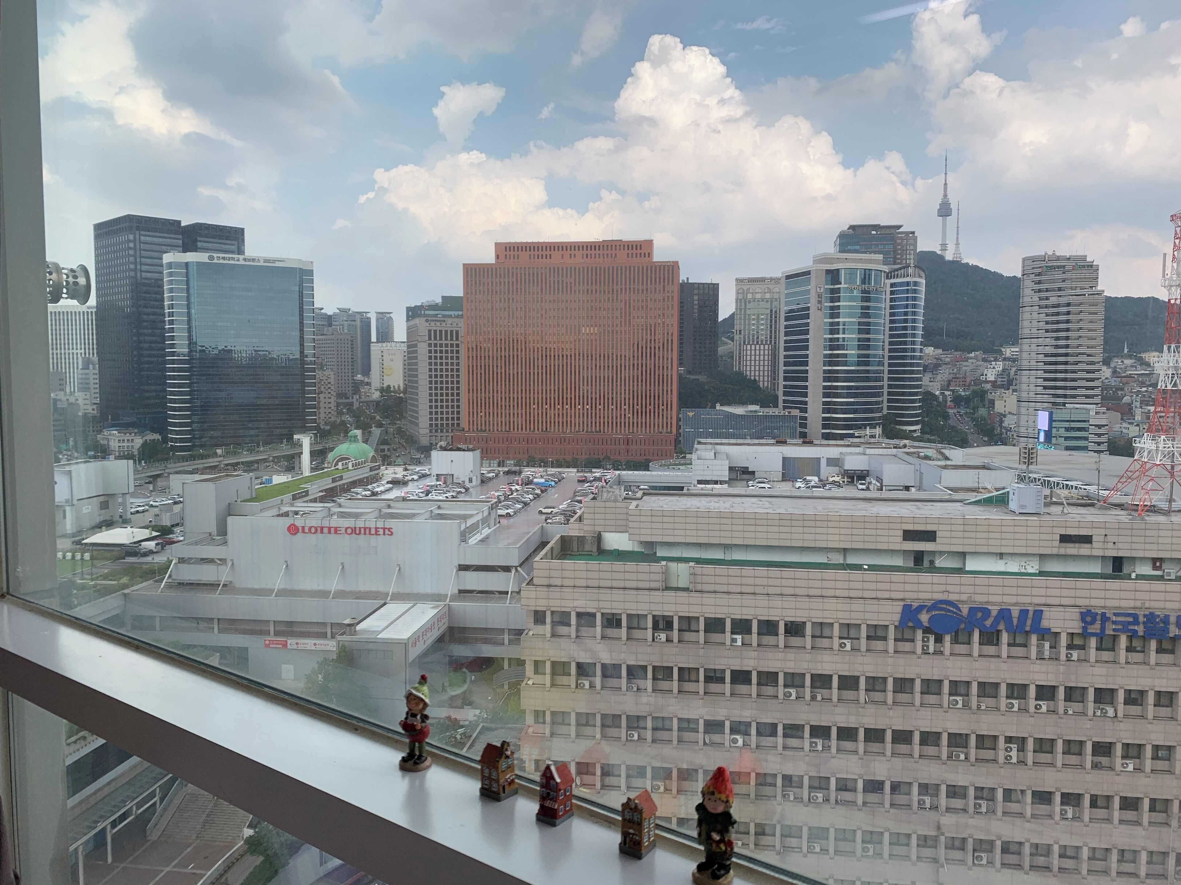 A cityscape with modern buildings, a large parking lot, and a building with a sign reading "KORAIL".