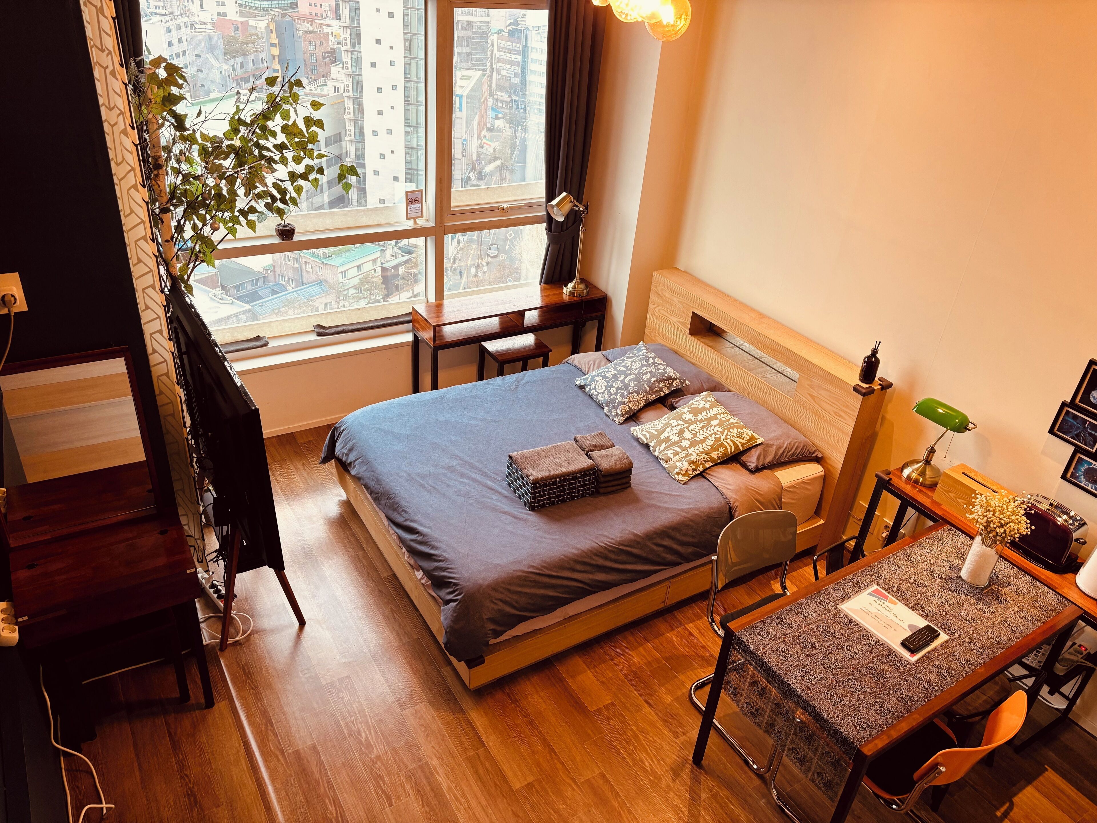Un hotel moderno con una cama grande, un escritorio de madera, una silla y vistas a la ciudad a través de amplias ventanas.