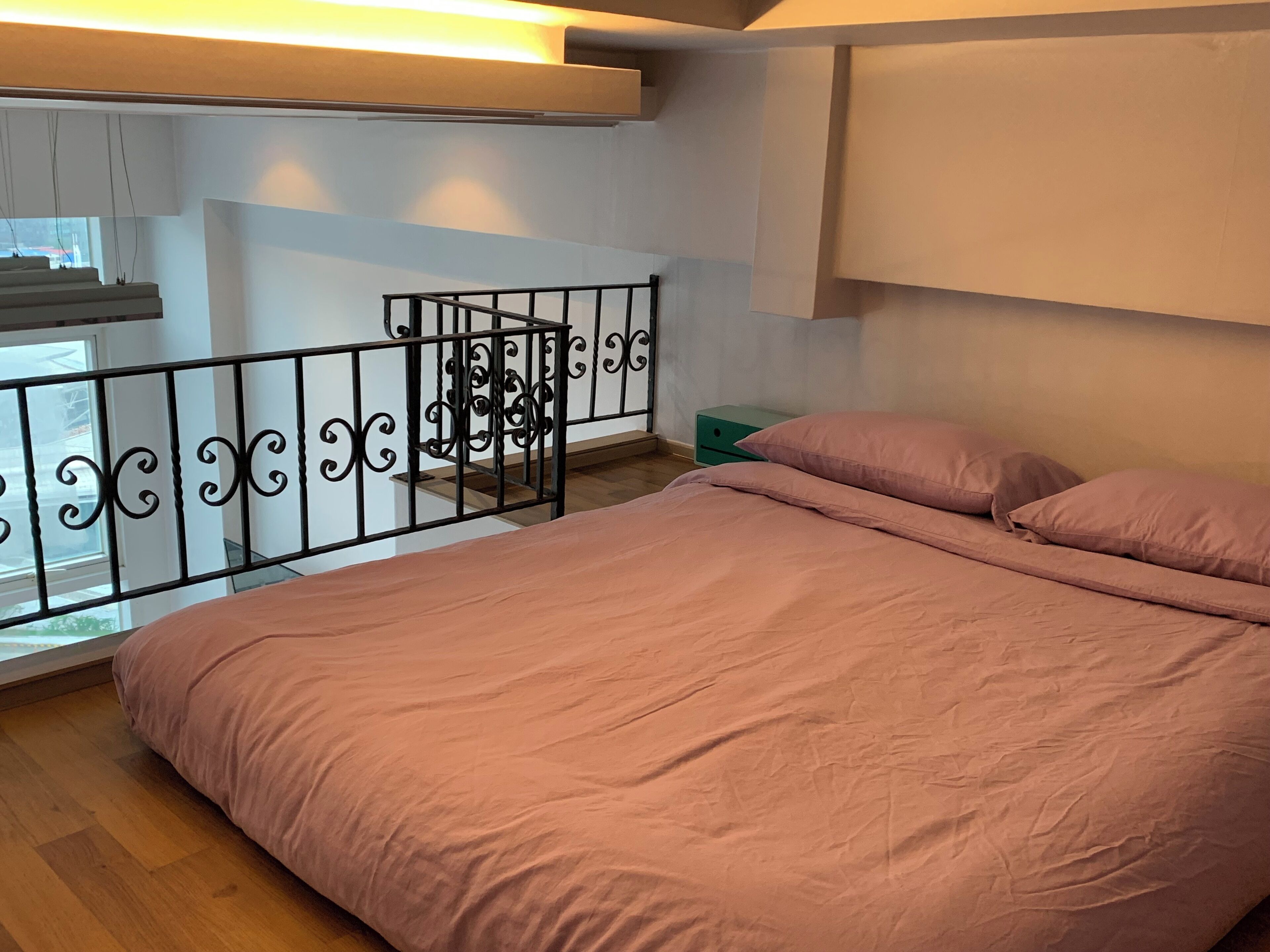 A bedroom with a bed, a balcony with a railing, a window, and a green storage box.