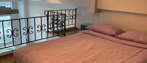 A bedroom with a bed, a balcony with a railing, a window, and a green storage box.