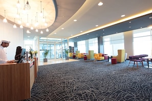 A modern hotel lobby with a reception desk, seating area, and large windows.