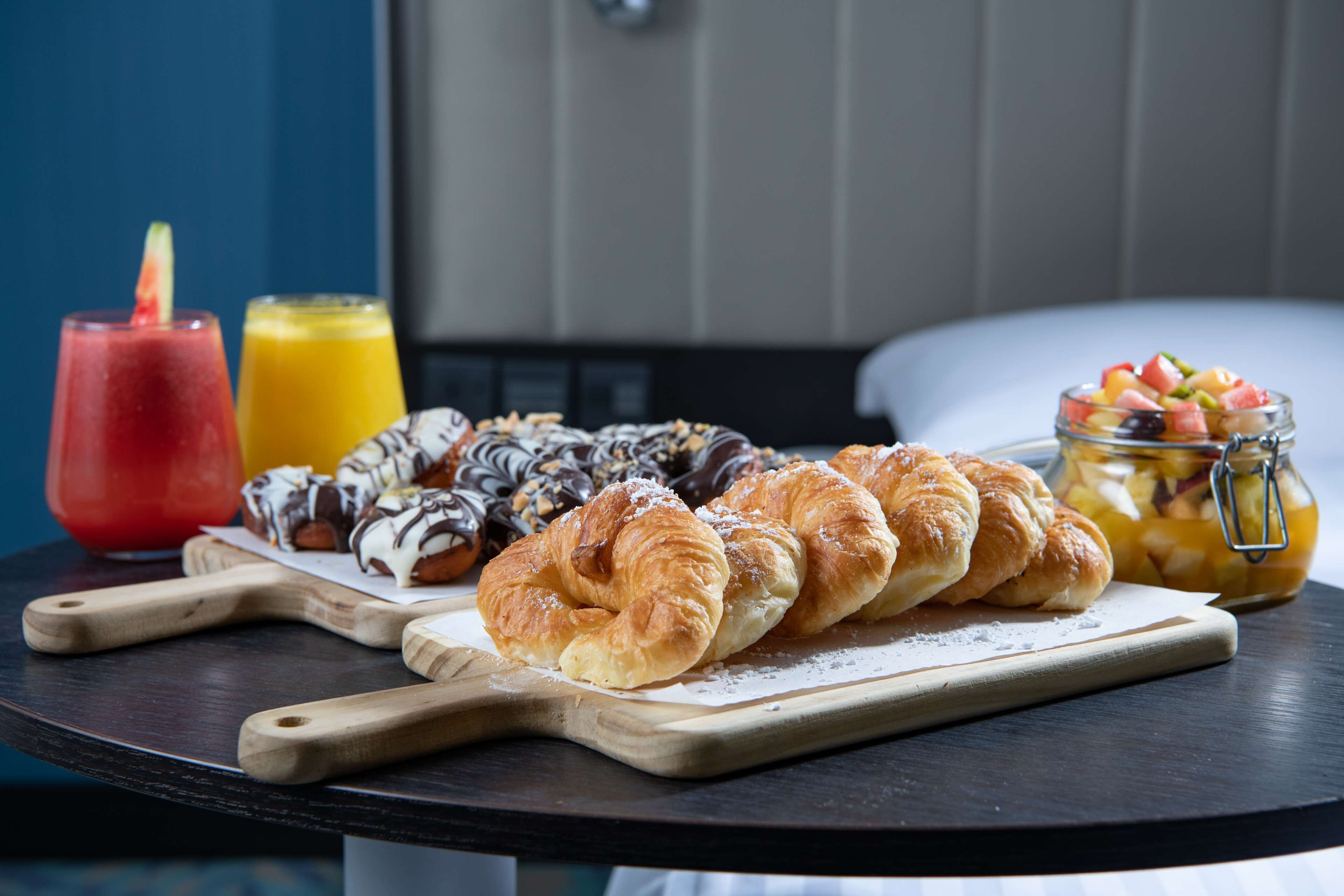 A breakfast table with croissants, a fruit jar, and two drinks.