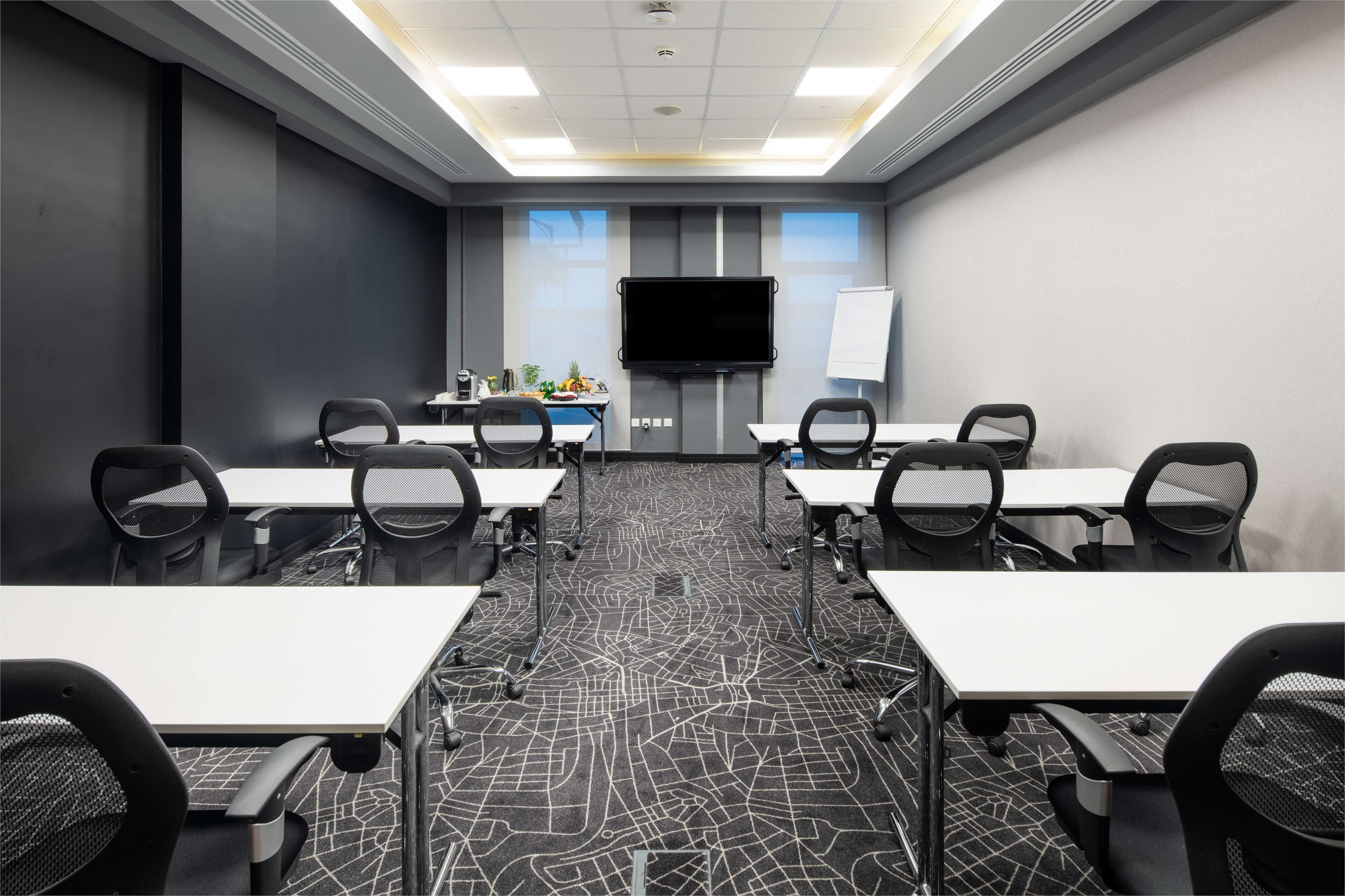 A conference room with a large flat-screen TV, whiteboard, and a carpet with a geometric pattern.