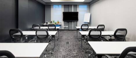 A conference room with a large flat-screen TV, whiteboard, and a carpet with a geometric pattern.