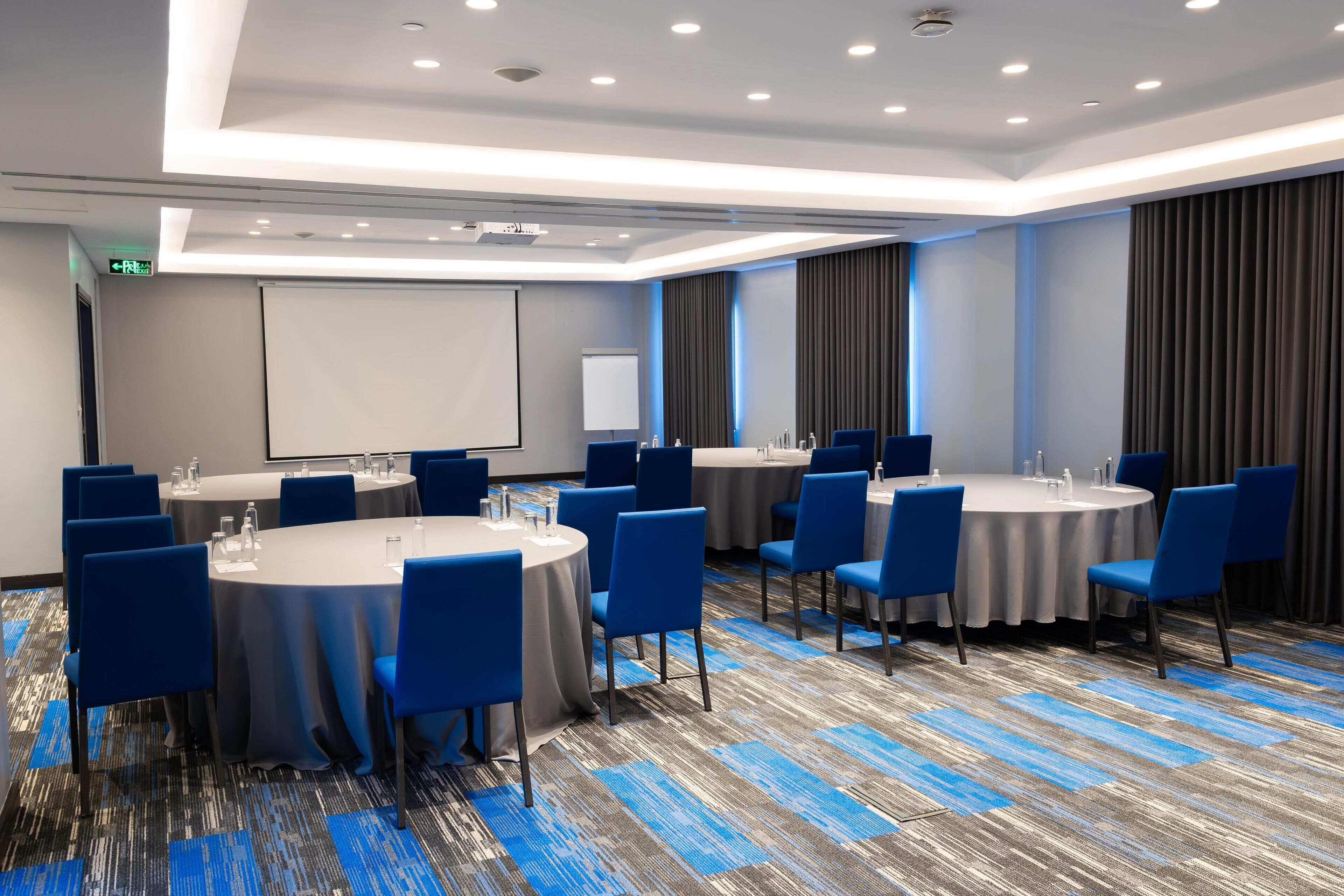A conference room with round tables, blue chairs, and a carpeted floor.