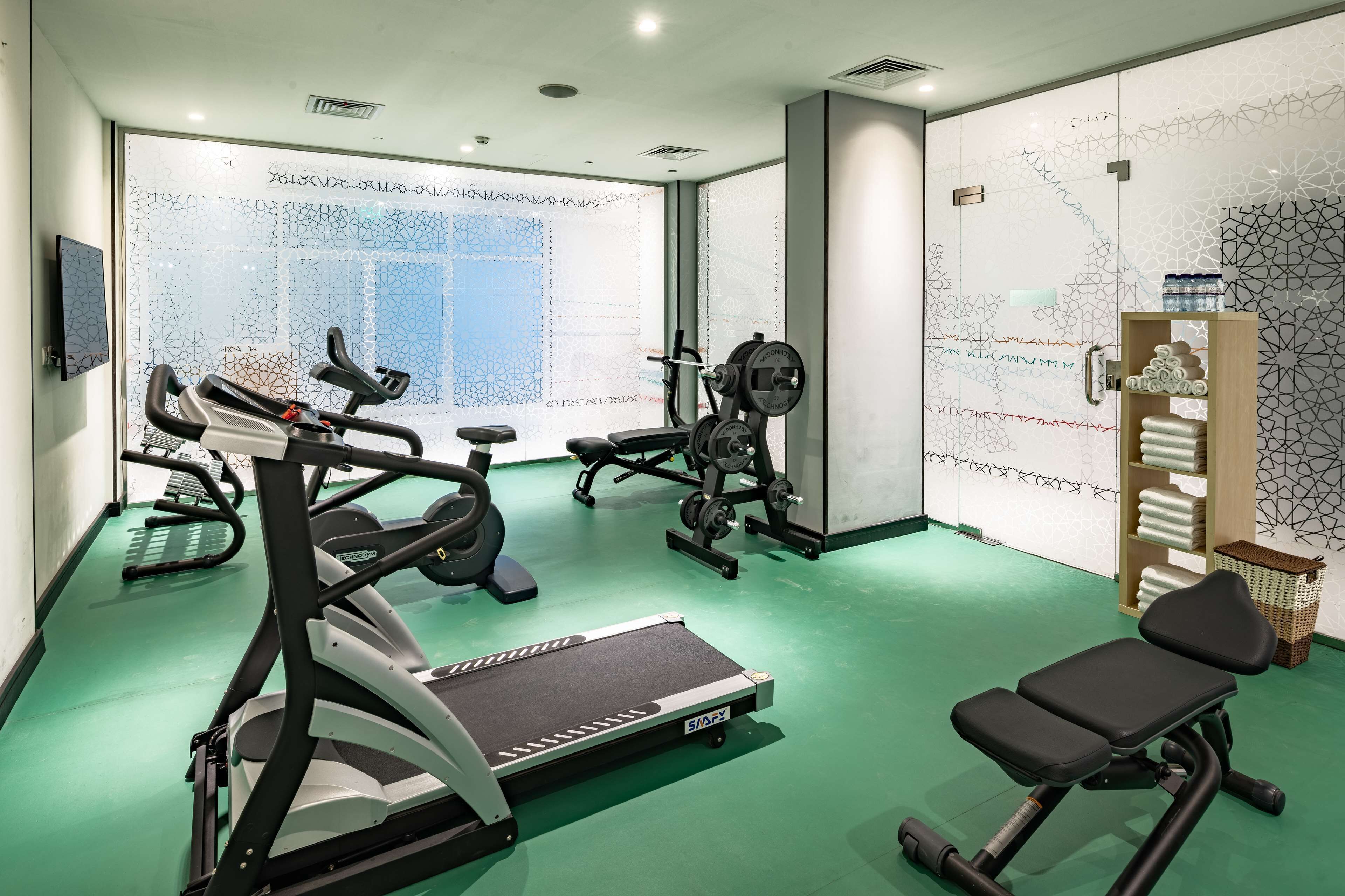 Une salle de sport équipée de matériel d’exercice, d’un banc et d’un mur recouvert de carreaux décoratifs.