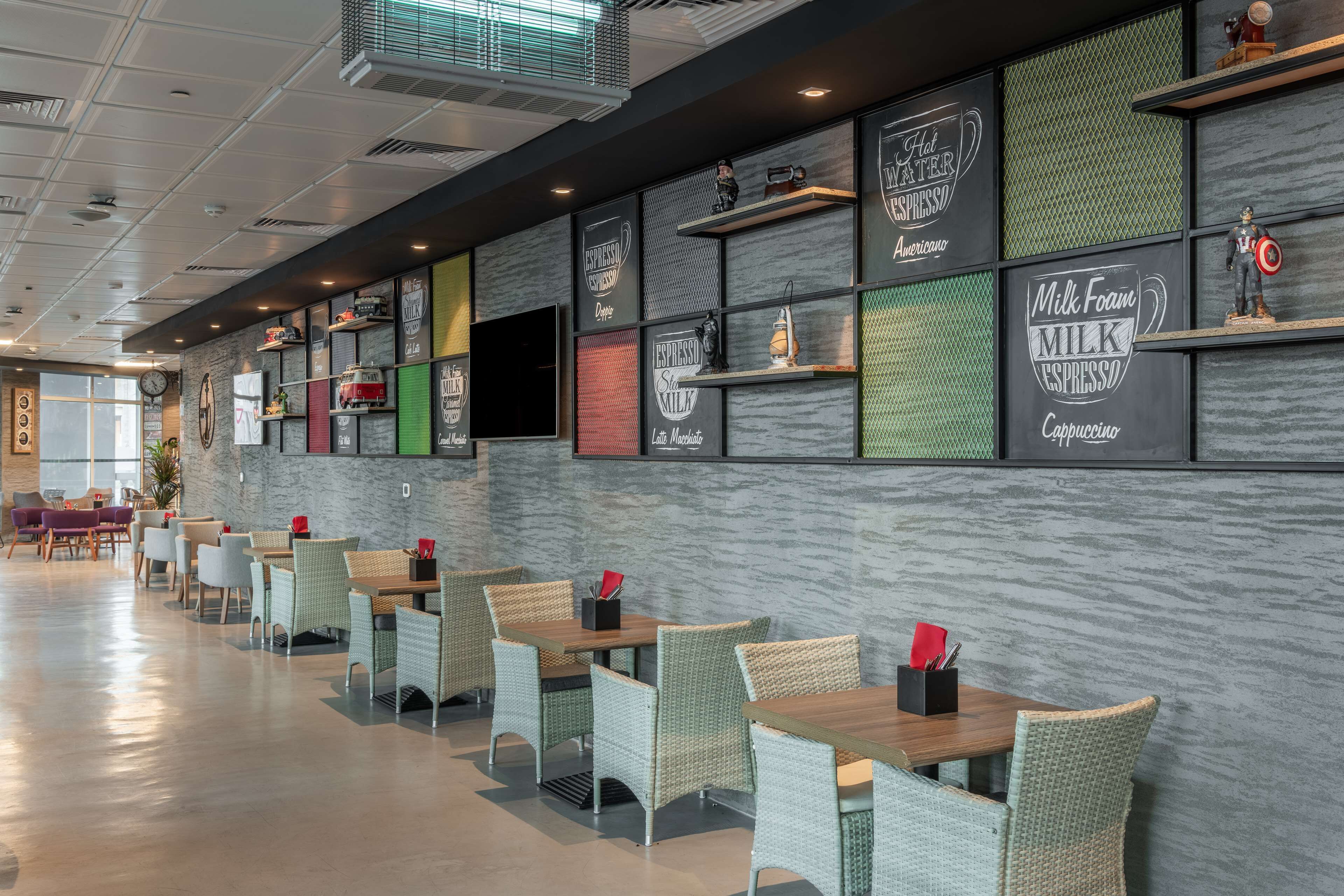 Un café moderne avec un long comptoir, des chaises en osier et un large choix de boissons affichées sur le mur.