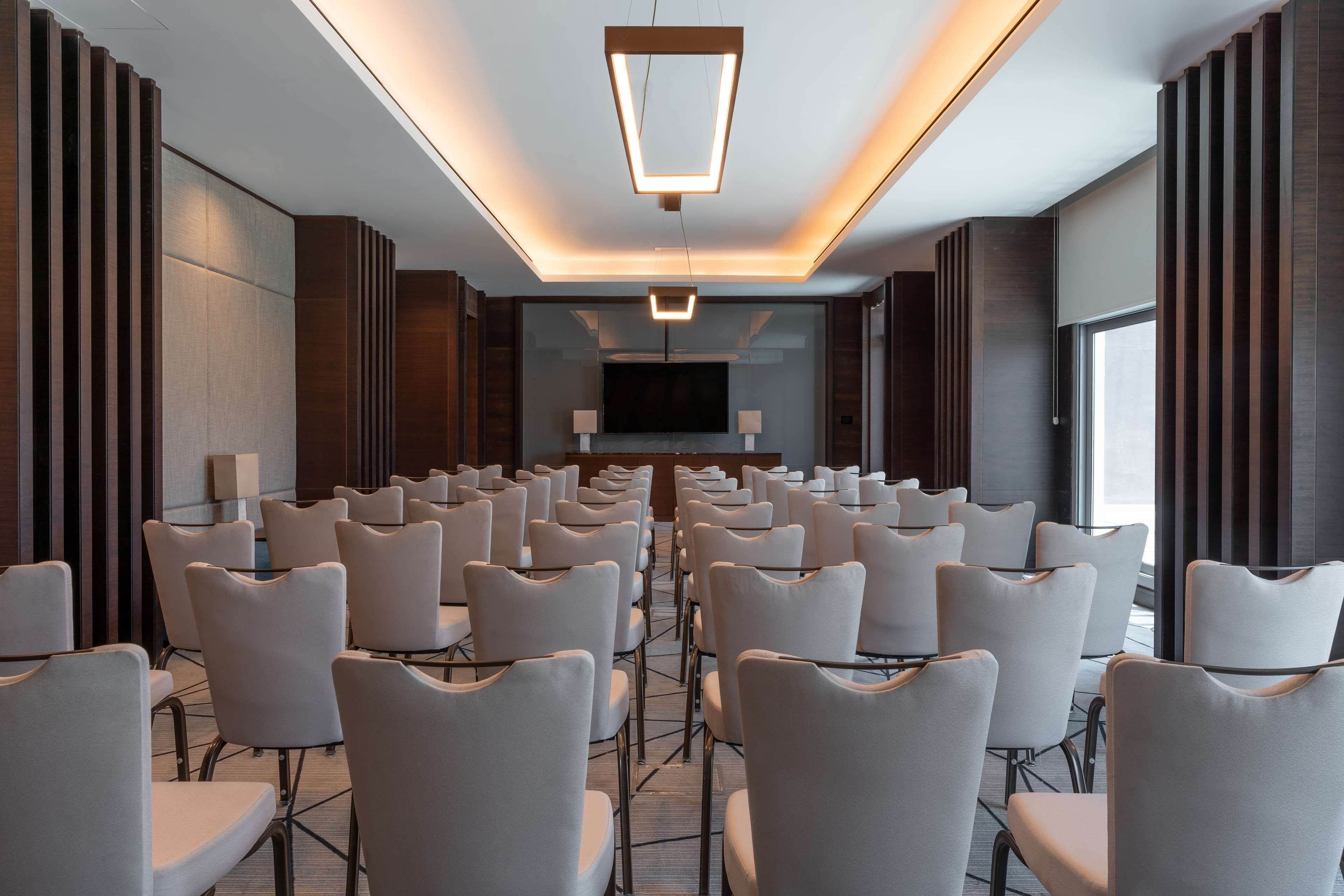 A conference room with rows of chairs, a large screen, and a modern ceiling design.