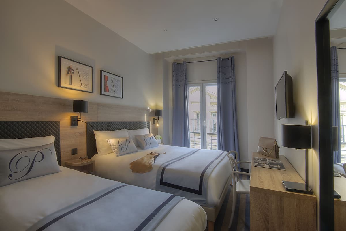 A hotel room with two beds, a desk, a chair, a TV, and a window with curtains.
