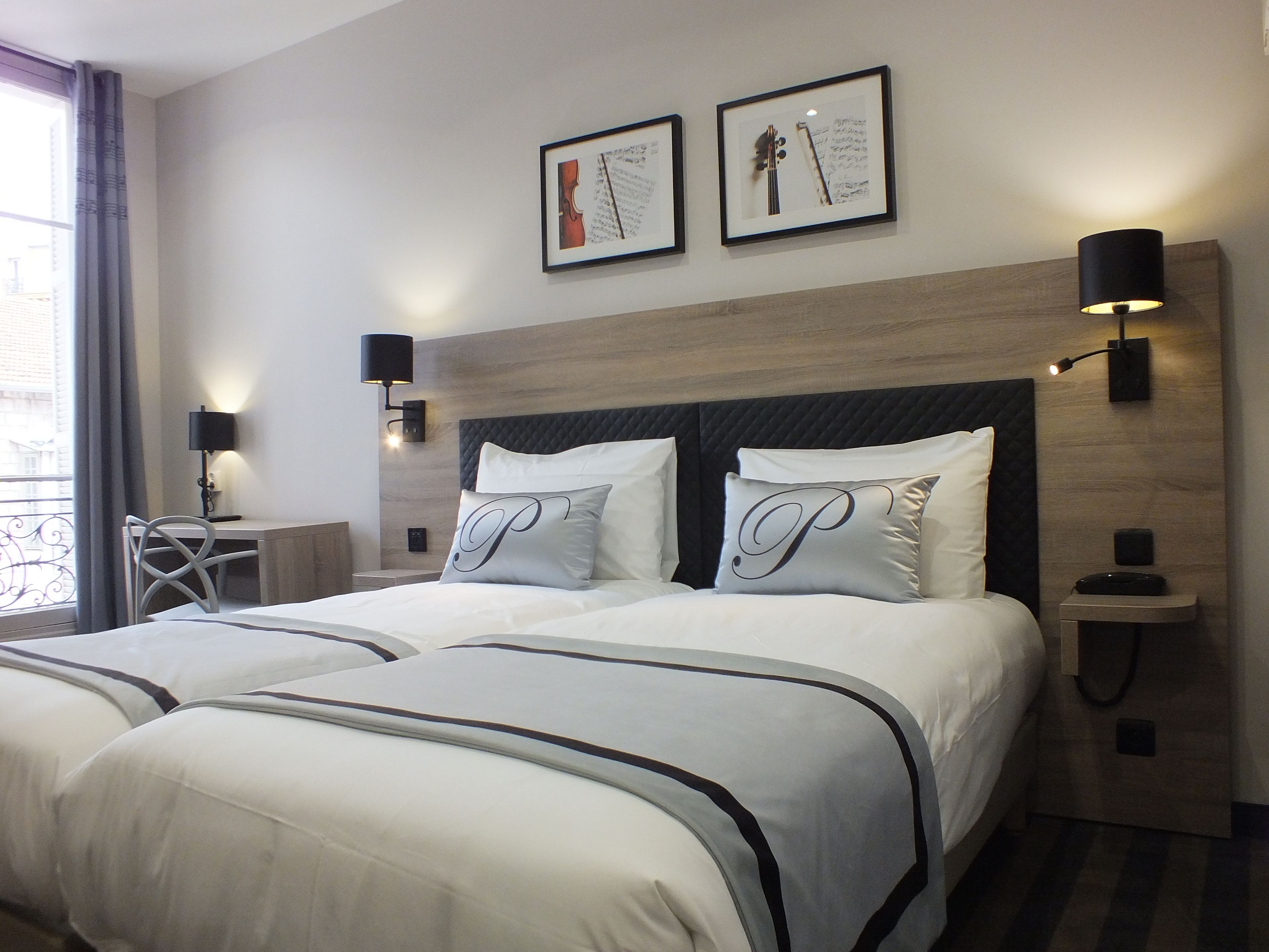 A hotel room with a large bed, two bedside tables, a desk, and a chair. There are two framed pictures on the wall and two wall-mounted lamps.