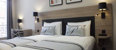 A hotel room with a large bed, two bedside tables, a desk, and a chair. There are two framed pictures on the wall and two wall-mounted lamps.