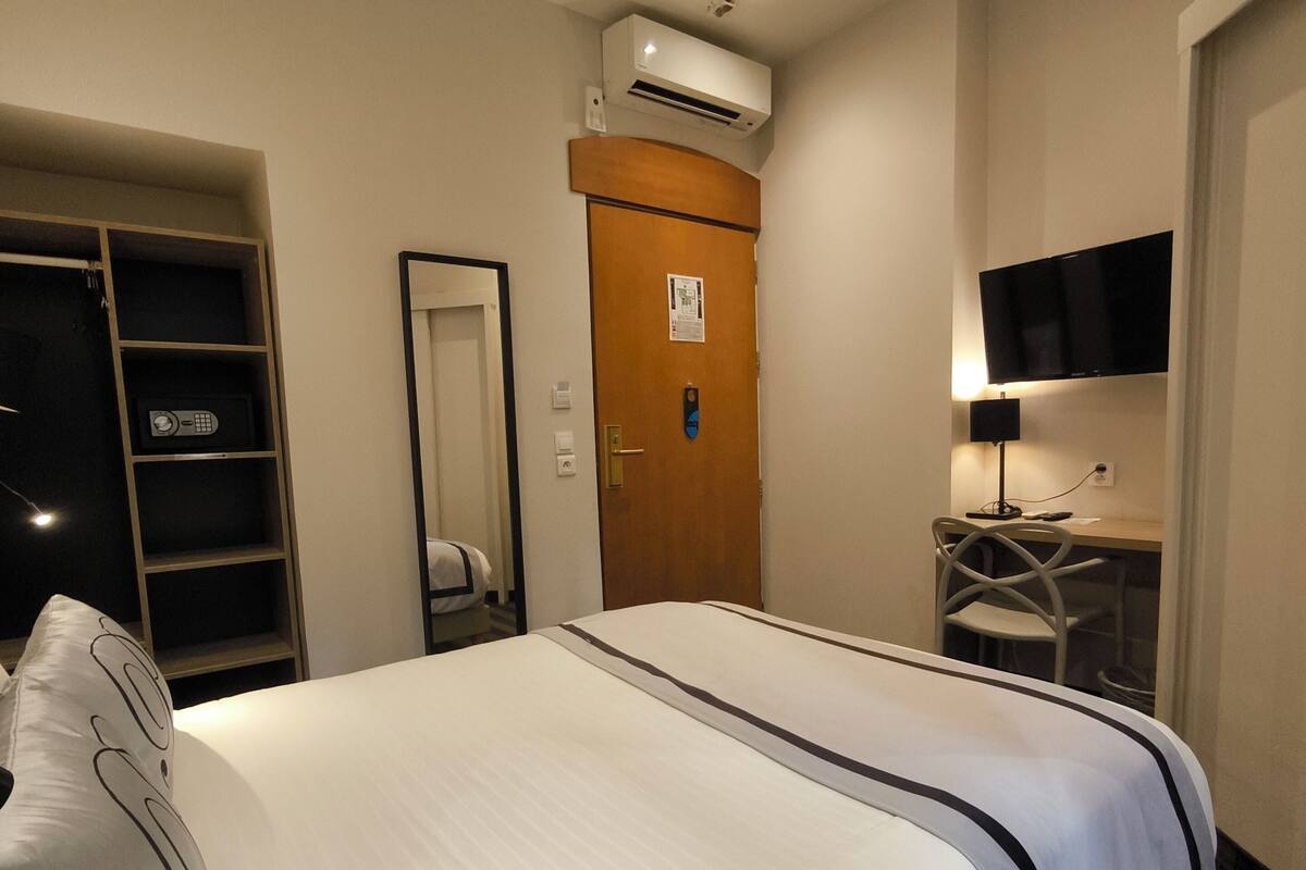 A hotel room with a bed, a desk, a chair, a TV, and a wardrobe.