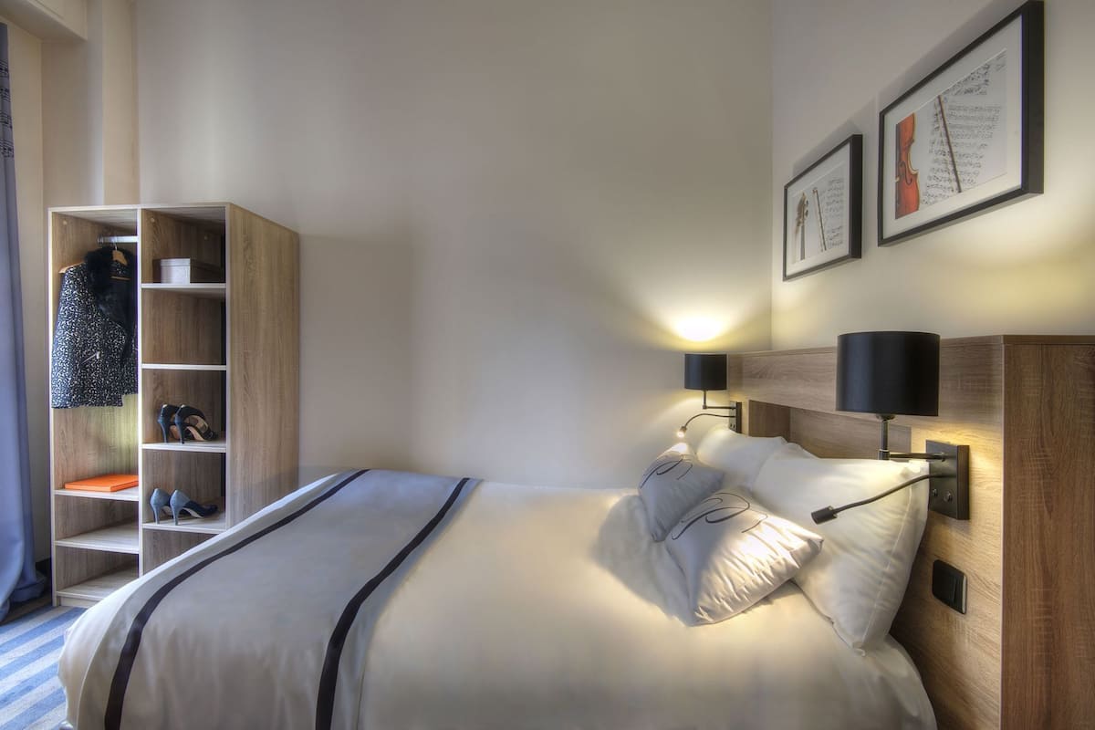 A hotel room with a bed, bedside lamps, a wardrobe, and framed pictures on the wall.