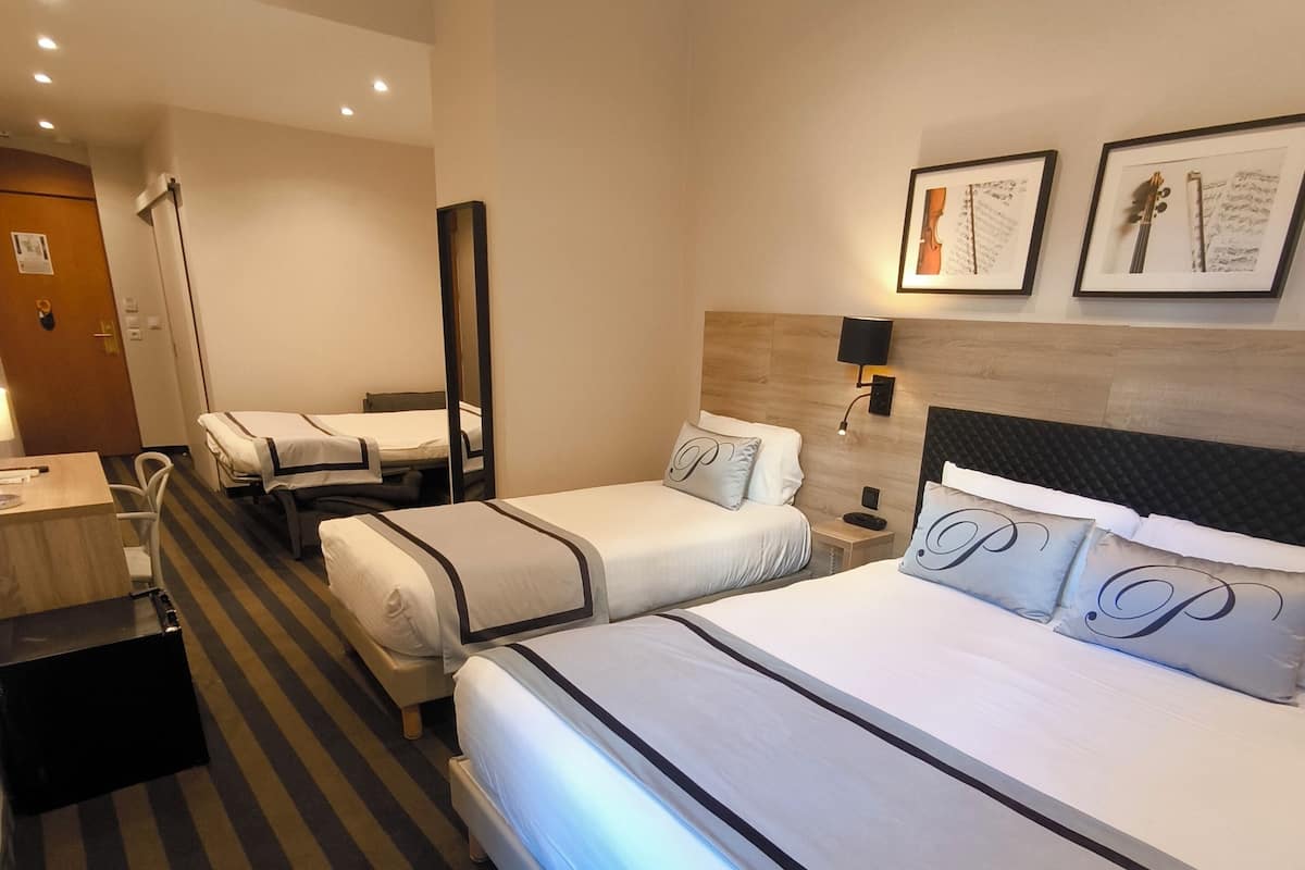 A hotel room with two single beds, a large bed, a desk, a chair, a mirror, and framed pictures on the wall.