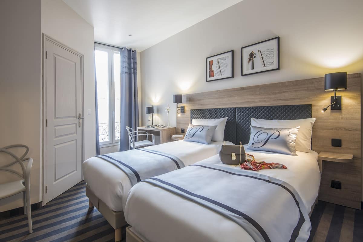 A hotel room with two beds, a desk, a chair, and a window with curtains.