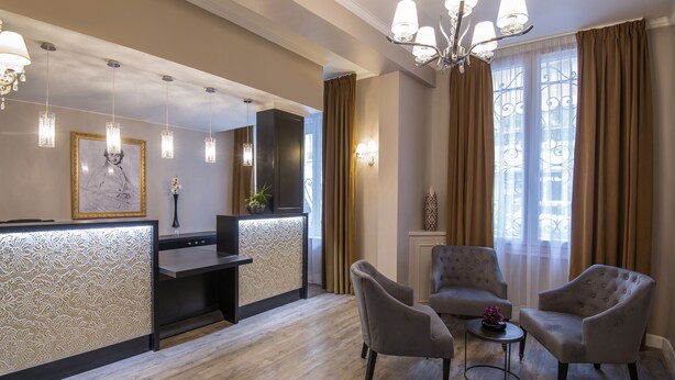 Een hotellobby met een receptiebalie, twee fauteuils, een bijzettafeltje en een kroonluchter.