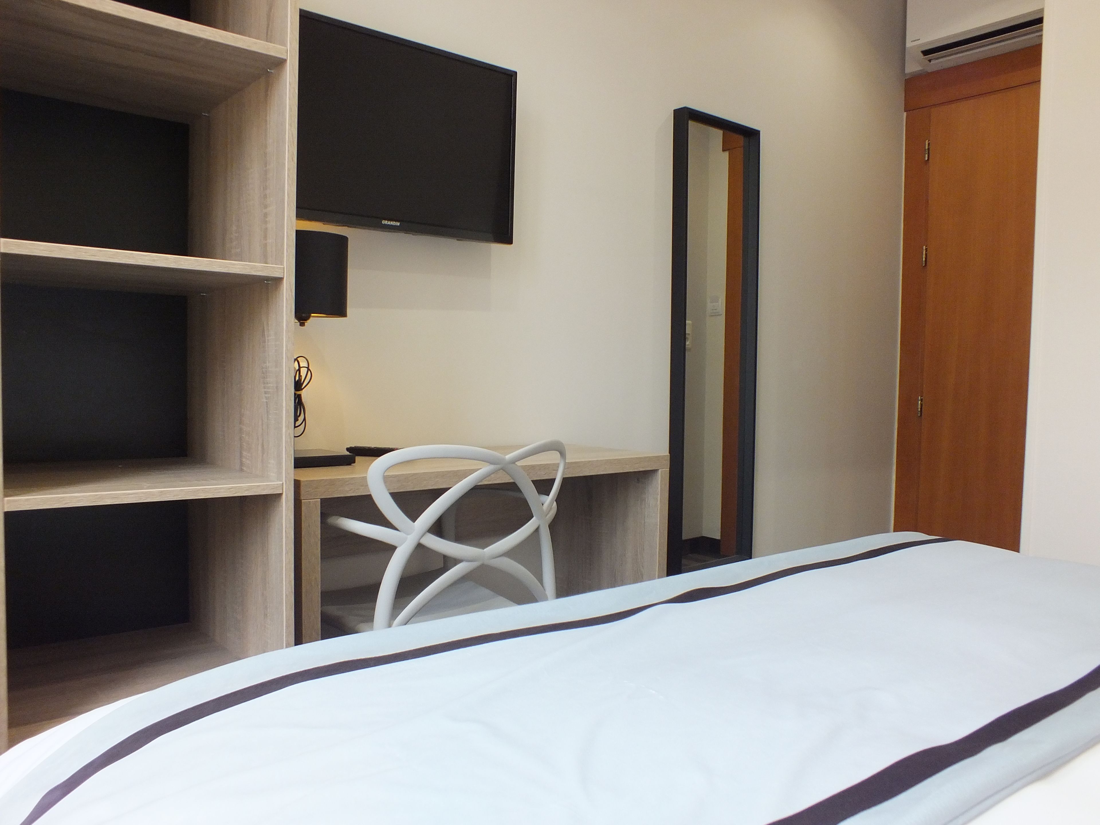 A hotel room with a bed, a desk with a chair, a television, and a wardrobe.