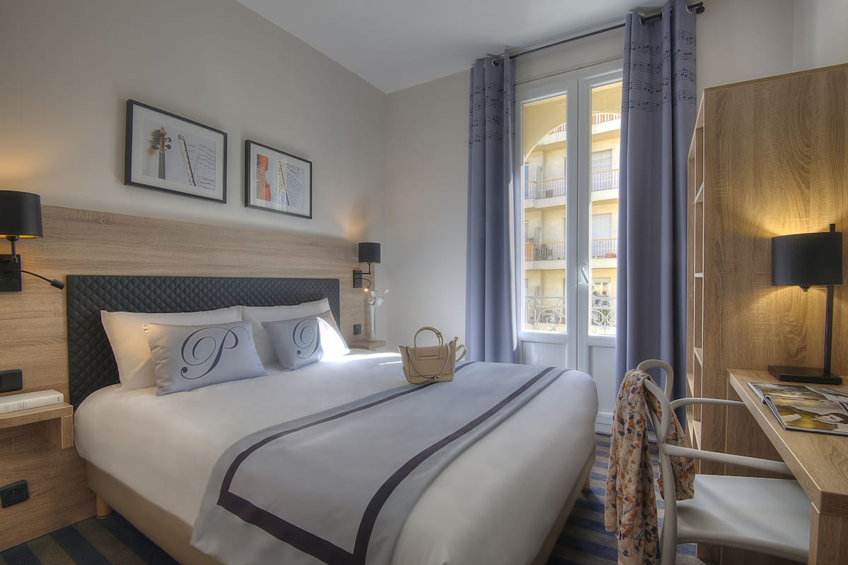 A hotel room with a large bed, a desk, and a view of the building's interior.