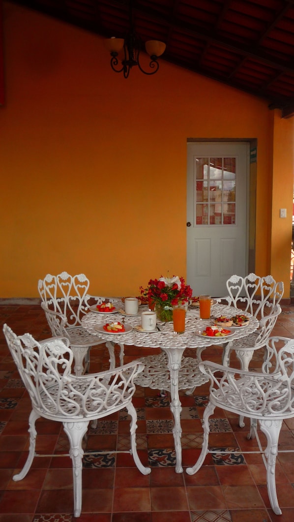 A dining area with a round table and white chairs, a vase with flowers, and a door in the background.