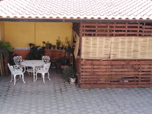 A patio with a round table and white chairs, surrounded by potted plants and a wooden fence.