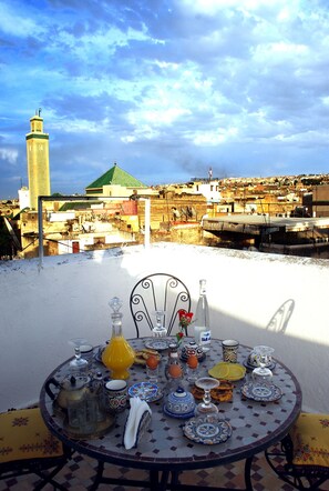 A table set with traditional Moroccan dishes and drinks, overlooking a cityscape with a prominent minaret. - Dar Ain Allo (Fes)