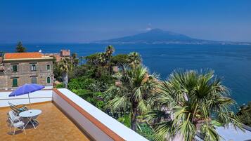 Una terraza con mesa y sillas, con vistas a la costa y una montaña al fondo.