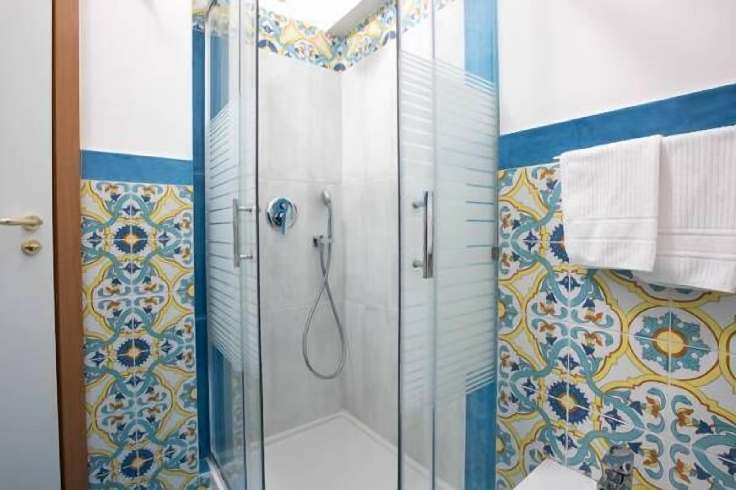 Eine Dusche mit Glastür, ein weißes Waschbecken und gemusterte Fliesen.