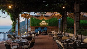 An outdoor restaurant with tables and chairs, a view of the sea, and a sign for 'Terrazza Glicine.' - Hotel Aequa (Vico Equense)