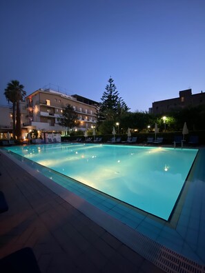 A swimming pool with lounge chairs and umbrellas, surrounded by buildings with balconies and lights. - Hotel Aequa (Vico Equense)