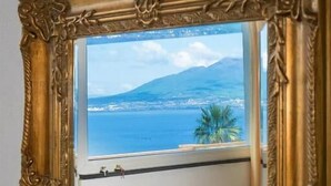 A room with a large ornate gold-framed mirror reflecting a view of the sea and mountains. - Hotel Aequa (Vico Equense)