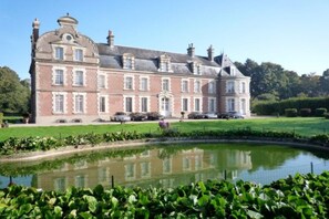 Ein großes, historisches Gebäude mit einer symmetrischen Fassade, einem zentralen Eingang und einem umlaufenden Garten mit Teich.