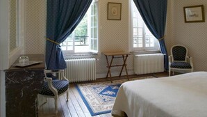 A bedroom with a bed, two chairs, a small table, and a radiator. - Château de Béhen (Behen)