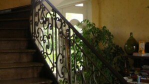 A wooden staircase with ornate black metal railings and a window at the top. - Château de Béhen (Behen)