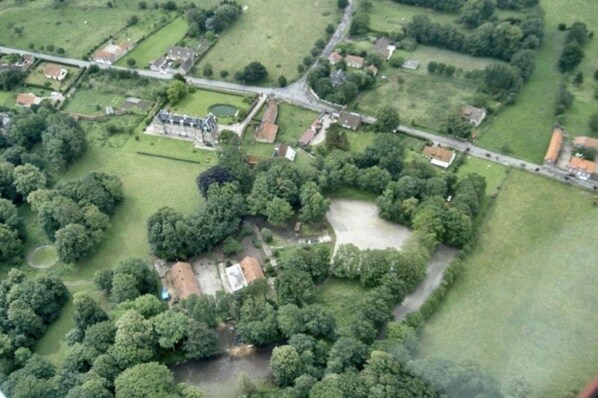An aerial view of a rural area with scattered houses, green fields, and a central building with a large open space. - Château de Béhen (Behen)