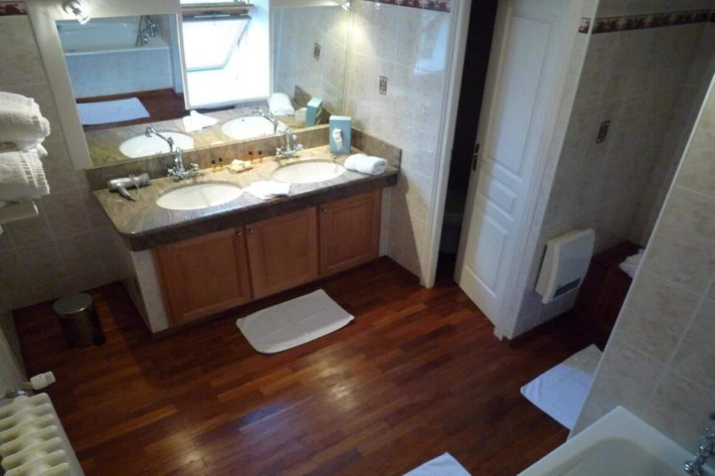 A bathroom with two sinks, wooden cabinets, a white towel on the floor, and a radiator.