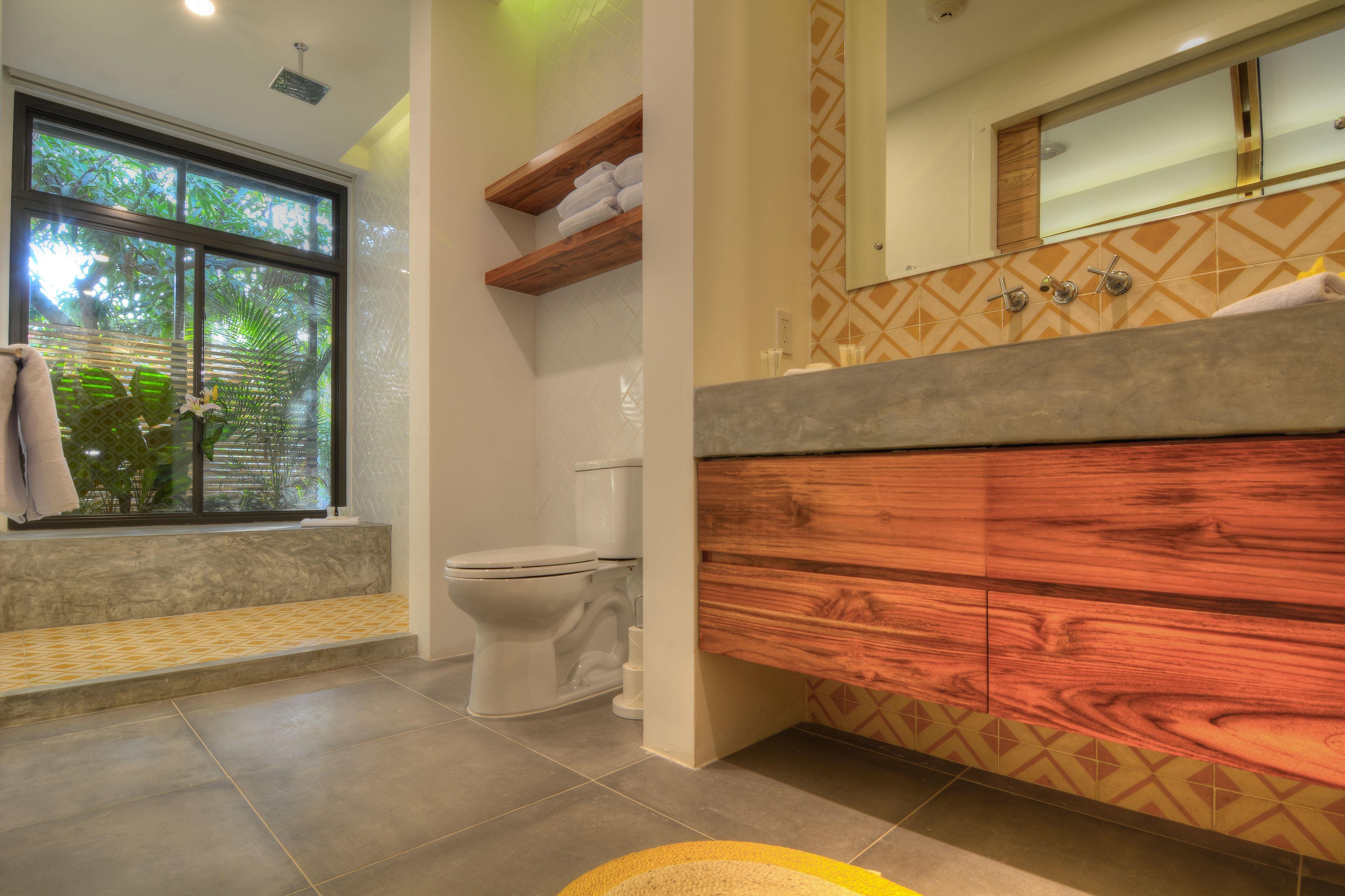 Une salle de bain avec des toilettes, un meuble-lavabo en bois et une fenêtre donnant sur un paysage verdoyant.