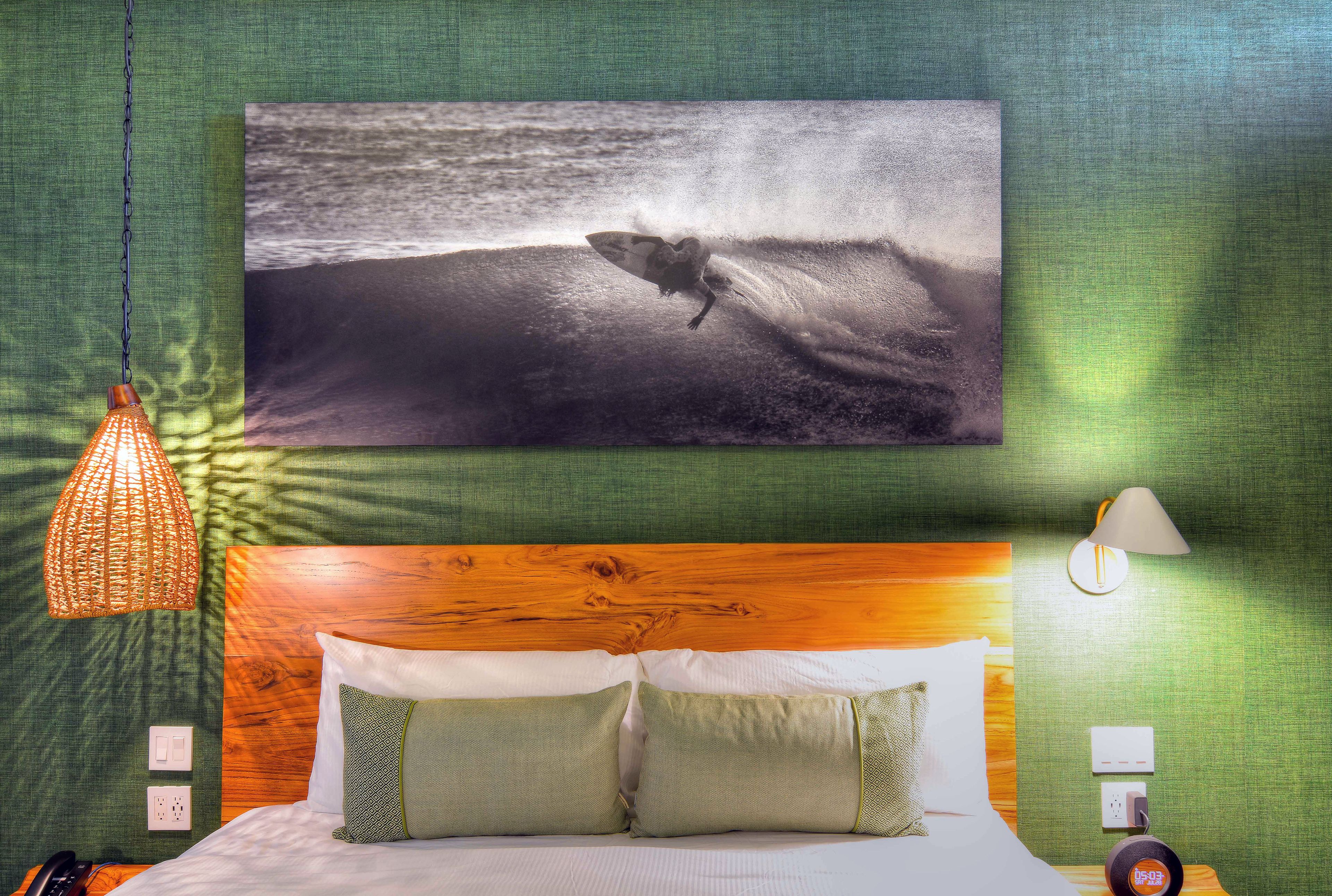 Ein Schlafzimmer mit Bett, Kissen, einer Hängelampe, einer Wandlampe und einem Gemälde, das einen Surfer zeigt.