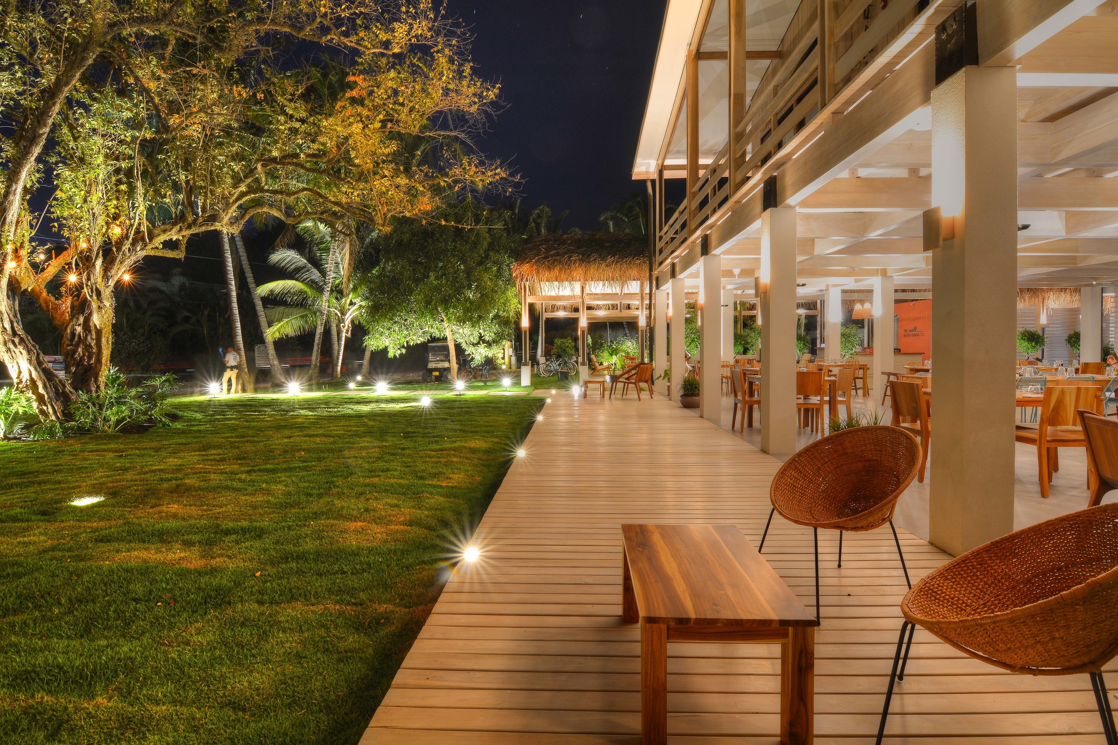 An outdoor patio area with wooden flooring, wicker chairs, and a thatched-roof structure.