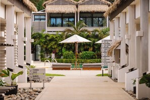 A resort entrance with a pathway leading to a pool area, surrounded by lounge chairs and a signpost indicating amenities like surf rooms, pool rooms, and a spa.