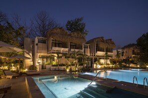 A modern hotel with a swimming pool, outdoor seating, and thatched-roof structures.