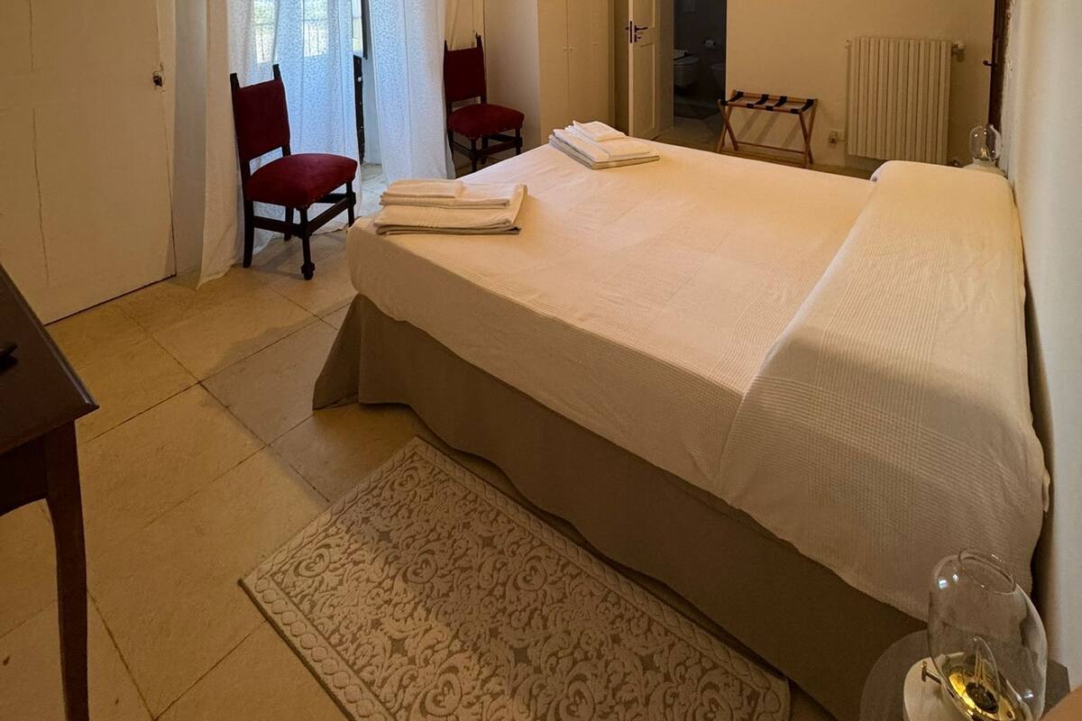 Un dormitorio con una cama grande, una silla, una mesita y un espejo.