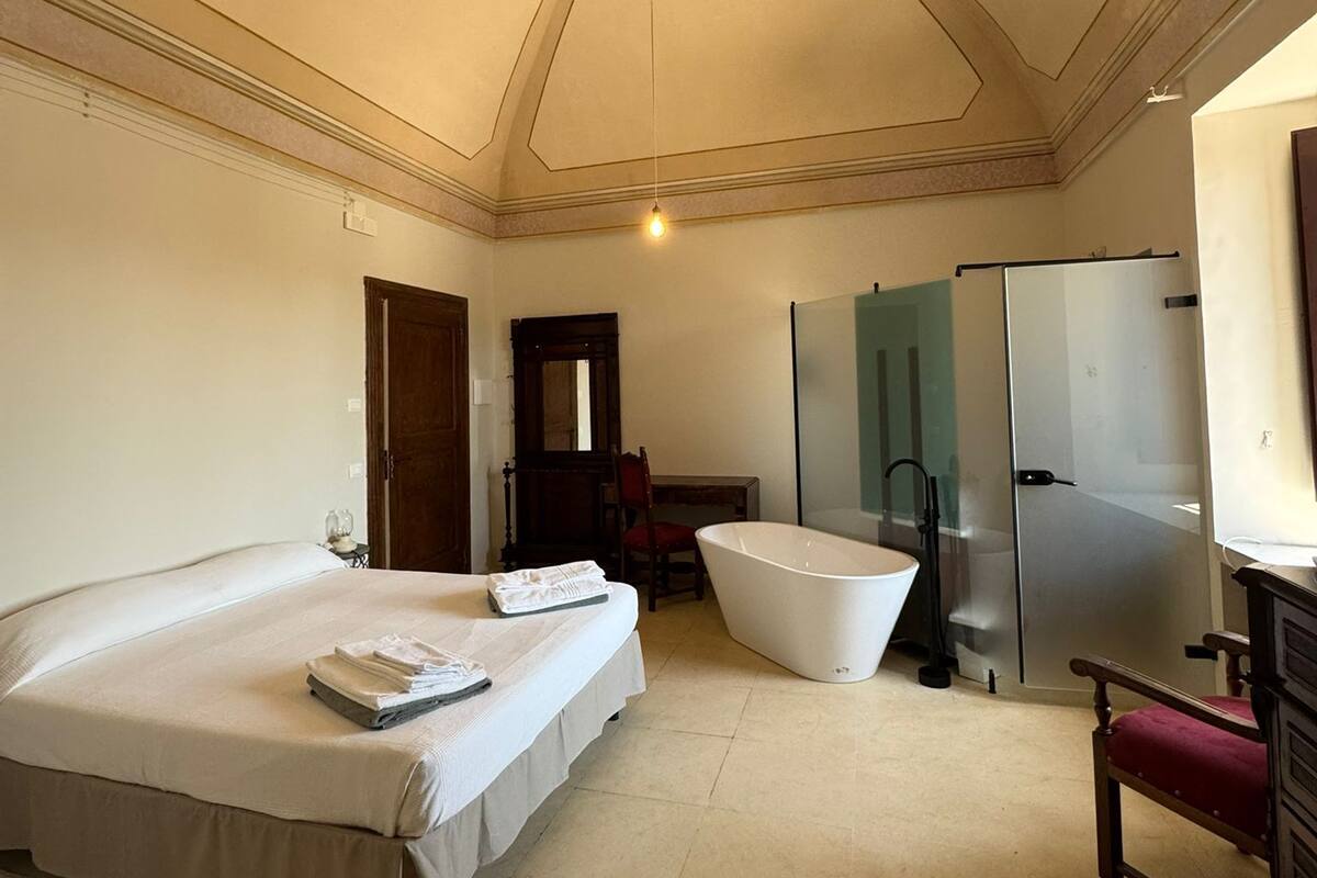 Habitación de hotel con una cama grande, una bañera, un refrigerador y un armario de madera.