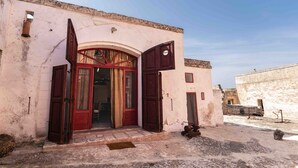 Un bâtiment doté d’une grande porte en arc de cercle, d’un petit porche et d’un mur de pierre en arrière-plan.
