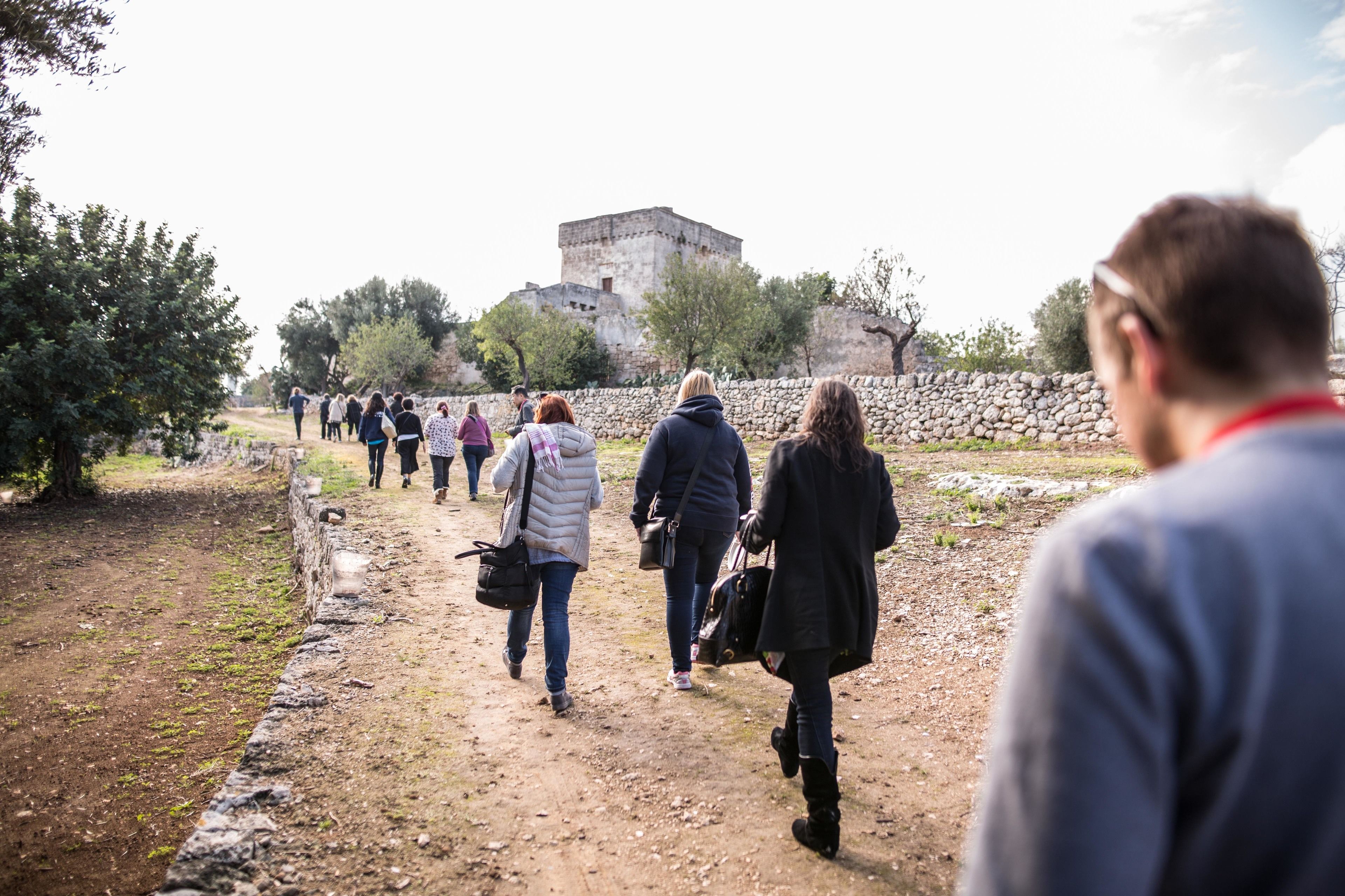 A group of people walking on a dirt path towards a stone building.