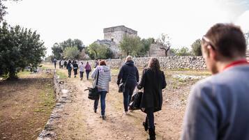 A group of people walking on a dirt path towards a stone building.