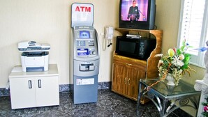 An ATM, a television, a microwave, a cabinet, and a glass table with a vase of flowers.